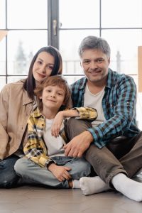 A smiling family sitting on the floor of their new home, enjoying a cozy moment.