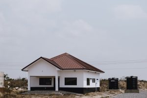 White modern house with brown roof in a rural setting, featuring water tanks.