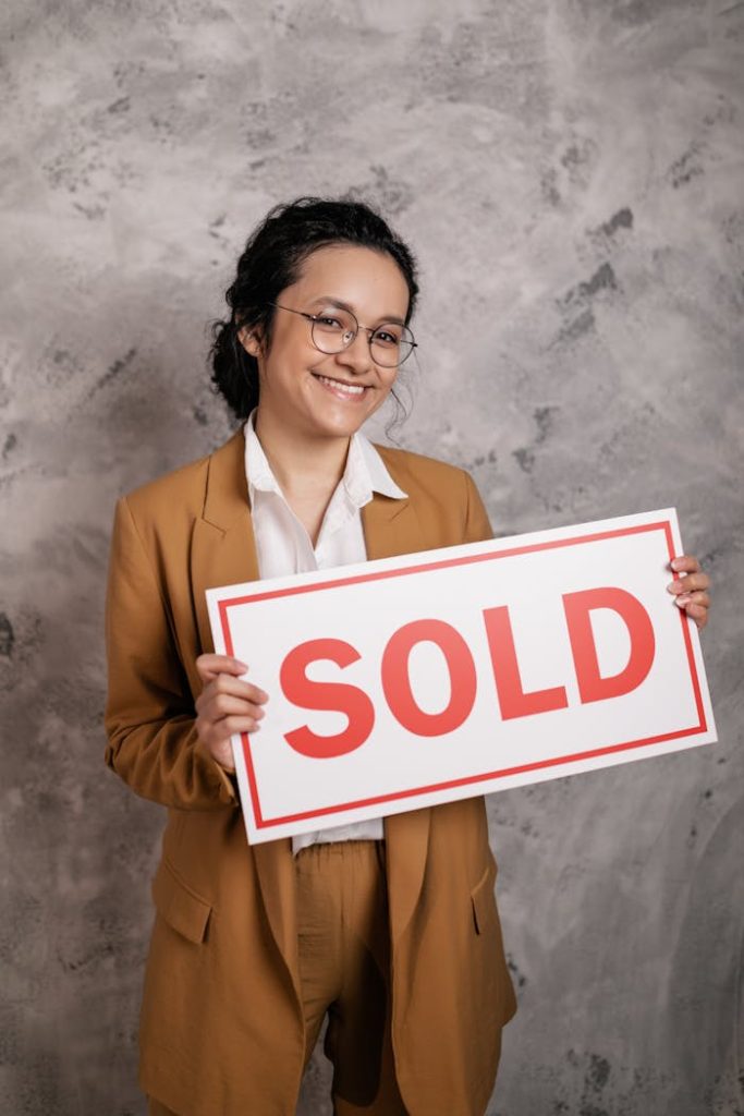 Smiling woman realtor holding a SOLD sign, symbolizing successful real estate deal.