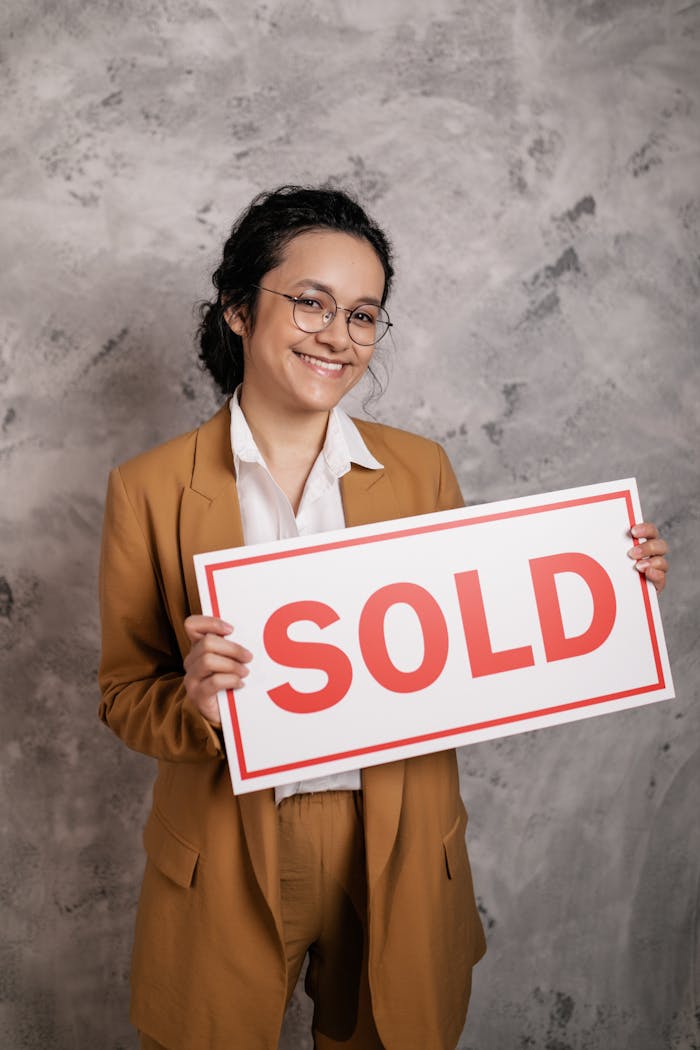 Smiling woman realtor holding a SOLD sign, symbolizing successful real estate deal.