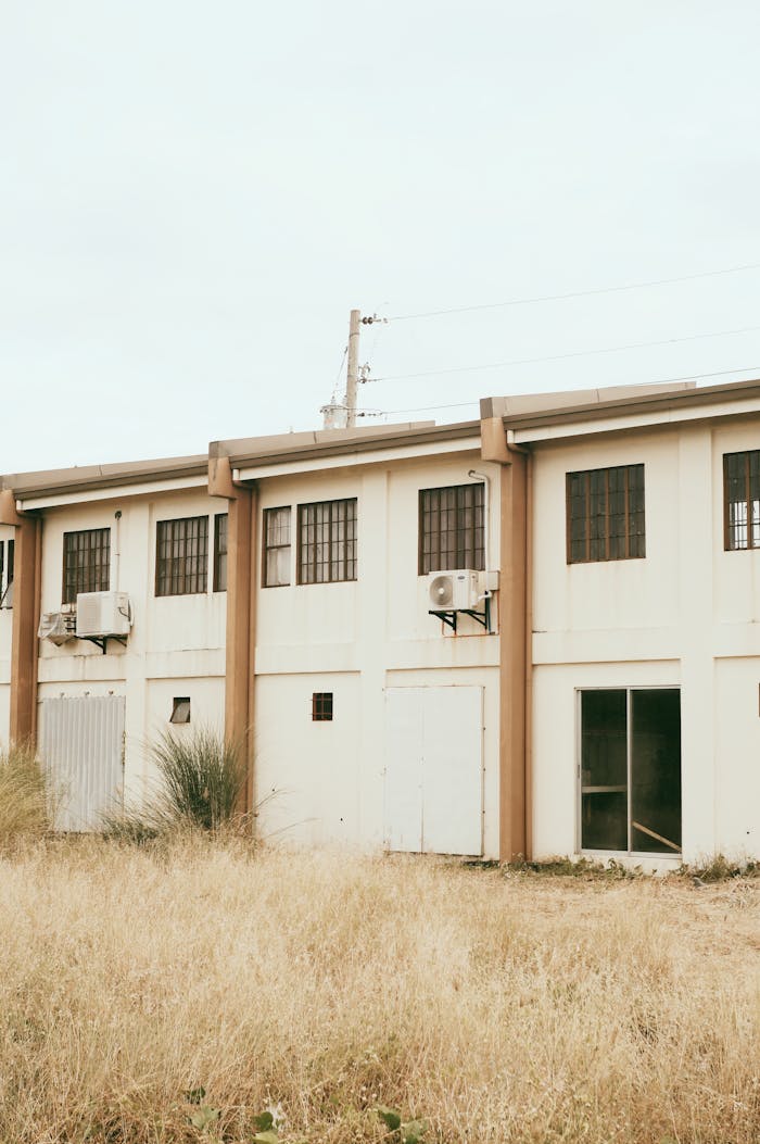 An exterior view of an abandoned building with overgrown grass in the foreground.